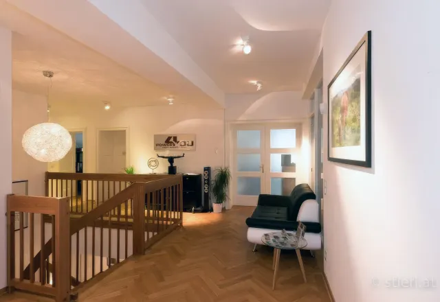Heller Wartebereich des Studios mit Holzparkett, schwarzem Ledersofa, Treppe und 'Power 4 You'-Schriftzug