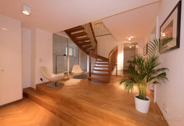 Offener, moderner Eingangsbereich mit Holzwendeltreppe, Parkettboden, zwei Design-Loungesesseln und einer Zimmerpflanze