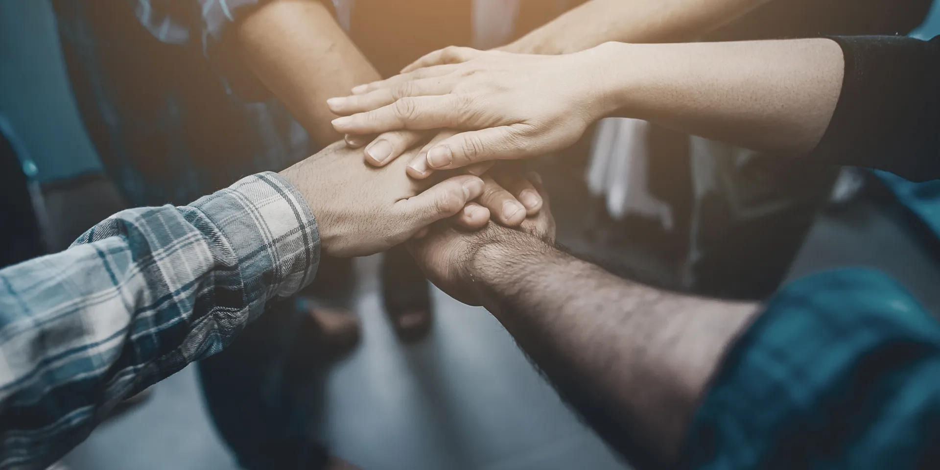 Nahaufnahme von mehreren Händen, die als Zeichen für Teamwork, Vertrauen und Zusammenarbeit in der Mitte aufeinanderliegen
