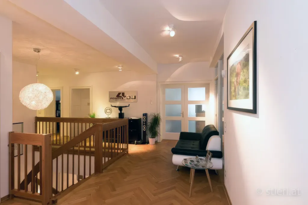 Heller Wartebereich des Studios mit Holzparkett, schwarzem Ledersofa, Treppe und 'Power 4 You'-Schriftzug