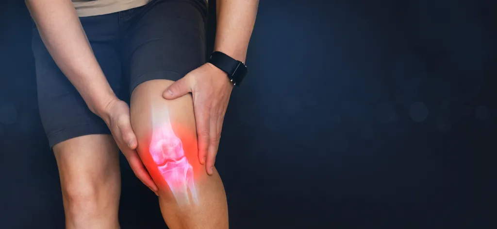 Nahaufnahme einer Person, die sich schmerzerfüllt das Knie hält mit rot leuchtender Kniegelenk-Illustration